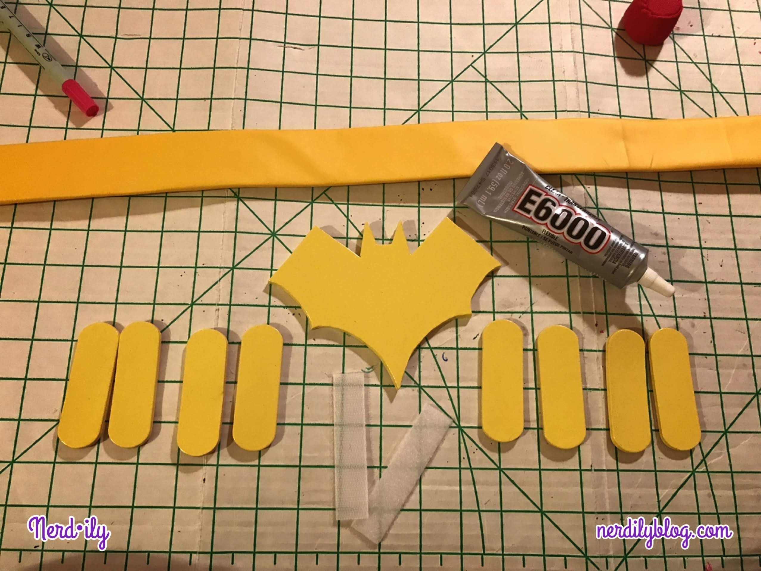 Yellow belt base on cutting board with a tube of E6000 glue, Batgirl symbol made of foam, and additional foam pieces. 
